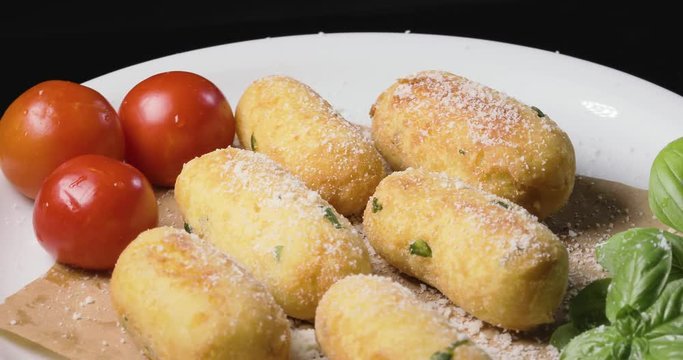 Crocchette di patate infarinate con prezzemolo disposte su un piatto bianco rotante con basilico e formaggio grattugiato. Dieta vegetariana e vegana.