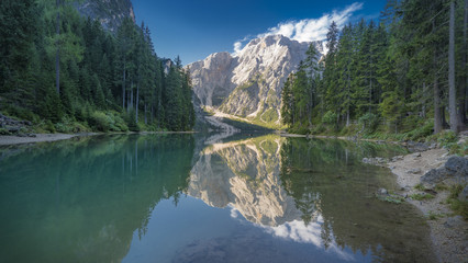 Pragser Wildsee mit sich spiegelnden Bäumen, Bergen und blauem Himmel 