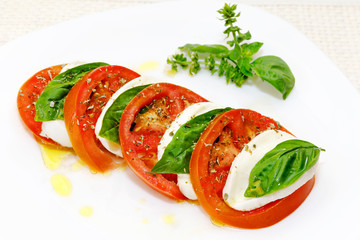 Caprese salad, slices of mozzarella and tomato, with basil and oregano.