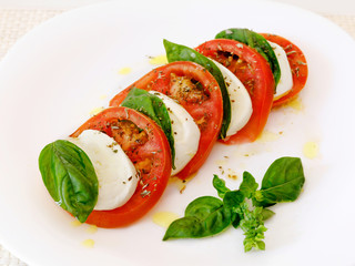 Caprese salad, slices of mozzarella and tomato, with basil and oregano.