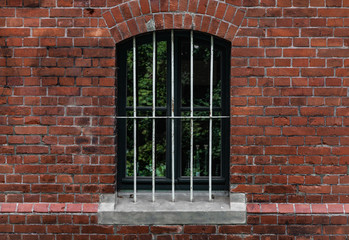 Fototapeta na wymiar Vergittertes Rundbogenfenster eines Backsteinhauses