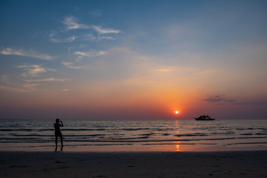 Silhouette of a man taking photos with mobile phone on the beach during sunset