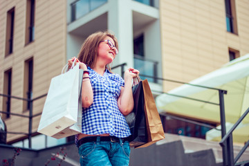 Content young lady after shopping holding up several bags. Low angle view of a young girl holding bags during the day