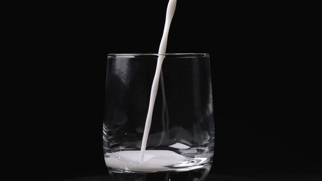 Latte versato nel bicchiere di vetro trasparente con sfondo nero. Super slow motion.
