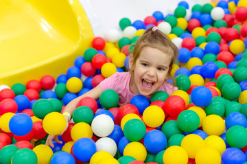 Fototapeta na wymiar Girl playing and having a good time in a ball room/ little smiling girl playing lying in colorful balls park playground/ Happy little girl having fun jumping into the ball pit with colorful balls.
