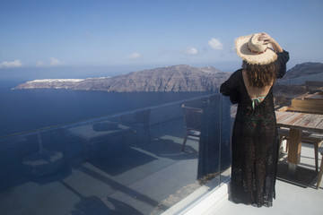 Beautiful woman with a hat enjoying amazing view of Santorini island. Summer Holidays in Greece.