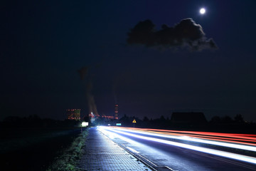 Światła samochodów w nocy i elektrownia w świetle księżyca w pełni.