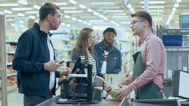 At the Supermarket: Checkout Counter Customer Pays with Smartphone for His Items. Big Shopping Mall with Friendly Cashier, Small Lines and Modern Wireless Paying Terminal System.