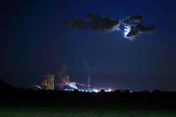 Elektrownia, fabryka w nocy w świetle księżyca w pełni za chmurą pary.