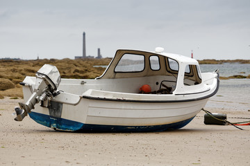 Fototapeta premium Bateau echoué sur une plage de Barfleur avec le phare de Gatteville en fond
