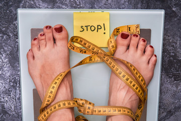 Stop Anorexia nervosa! Society perception, pressure about weight problem. Skinny female feet on a scale with yellow measuring tape. Loss weight social stigma. Body  positive concept.