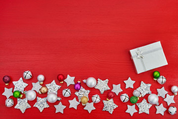 Christmas greeting card. Gift box and Christmas silver decoration on red background. Top view, copy space.