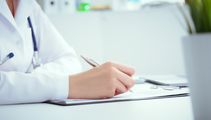 Front view of female doctor holding silver pen filling patient history list at clipboard pad. Physical exam or disease prevention.