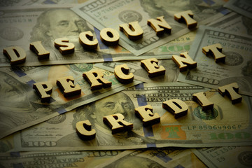 DISCOUNT, PERCENT, CREDIT is laid out of wooden letters on the background of hundred-dollar bills. Toning. Vignetting. The concept of financial transactions and bank loans.