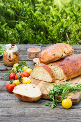 Fresh bread on wooden ground. Yellow tomato and red tomatoes with arugula. Feta cheese with olives and sundried tomatoes. Picnic, dinner outdoor. Still life of food.