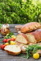 Fresh bread on wooden ground. Yellow tomato and red tomatoes with arugula. Feta cheese with olives and sundried tomatoes. Picnic, dinner outdoor. Still life of food.