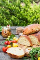 Fresh bread on wooden ground. Yellow tomato and red tomatoes with arugula. Feta cheese with olives and sundried tomatoes. Picnic, dinner outdoor. Still life of food.