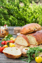Fresh bread on wooden ground. Yellow tomato and red tomatoes with arugula. Feta cheese with olives and sundried tomatoes. Picnic, dinner outdoor. Still life of food.