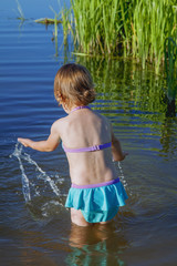 Little child girl splashing water in the lake. Holiday, vacation and health concept.