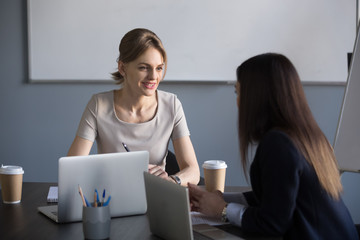 Millennial businesswomen working at laptop negotiating about future partnership, female partners talking during boardroom meeting, colleagues discussing company projects, sharing ideas in office