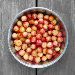 metal bowl with colored cherries in water on a wooden table background, top view, square frame