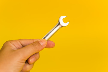 hand holding steel wrench on yellow background