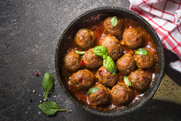 Meatballs in tomato sauce in a frying pan on dark stone table. 