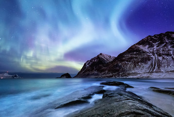 Aurora borealis on the Lofoten islands, Norway. Green northern lights above mountains. Night sky with polar lights. Night winter landscape with aurora and reflection on the water surface. 