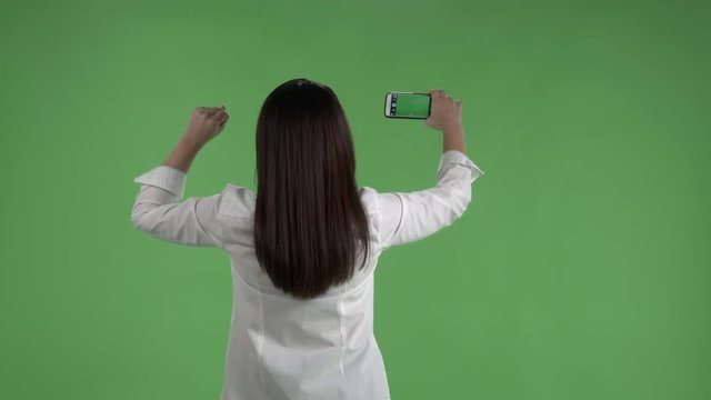 woman with raised fist taking pictures with camera phone against a green screen