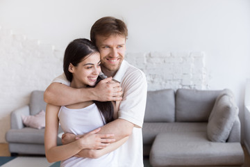 Portrait of happy young couple hugging looking in distance thinking about future family together, smiling boyfriend embracing girlfriend holding her in his arms dreaming about new beginning