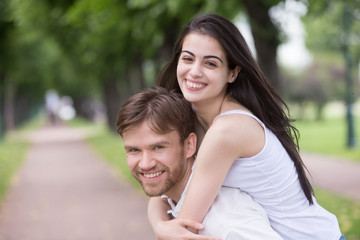 Naklejka premium Portrait of smiling young girlfriend piggyback millennial boyfriend during romantic walk in park alley, excited couple looking at camera have fun outdoors, playing foolish, man carry lover on his back