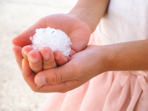 Young anonymous girl with hands filled with granulated hail ice crystals, wearing pink dress and shirt