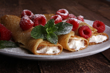 Homemade crepes served with fresh raspberrries and powdered sugar on rustic wooden table