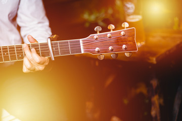 Guitar with a man's male hands playing the guitar on wooden wall background, electric or acoustic guitar with nature light. Concept of guys boys band performing on events 