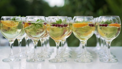 Three colorful cocktails in large wine glasses in a classic bar environment with dozens of blurry liquor bottles in the background.