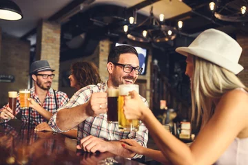 Young cheerful people in the beer pub drinking and having good time. Friendship concept with young people enjoying time together and having genuine fun at cool vintage pub 