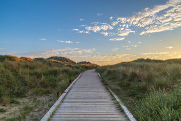 A wooden pathway leading towards the sea at Formby in Merseyside, taken at sunset - Powered by Adobe