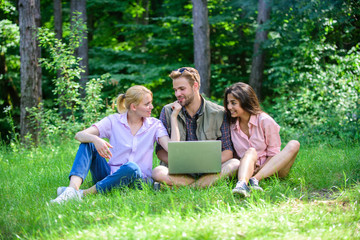 Company youth spend leisure outdoors with laptop. Friends working with laptop at green meadow....