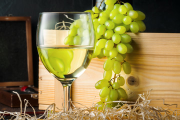 White wineglass and white yellow green bunches of berry grapes with bottle of wine corkscrew for cork on table in winery Concept food agriculture harvesting winemaking autumn summer.