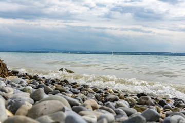 Strandufer mit bunten Steinen am Bodensee. Sommertag am Bodensee mit Mini Wellen.