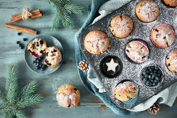 Blueberry muffins with sugar icing in a baking tray with Christmas decorations around, top view