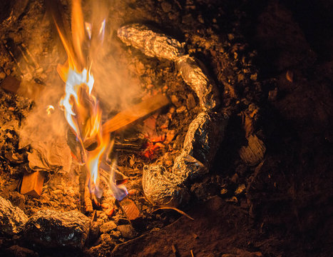 Tin Foil Wrapped Potatoes Cooking By The Side Of Bonfire During Camping. Long Exposure Shot Of Fire