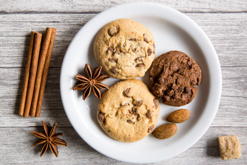 Tasty cookies with chocolate crumbles and chocolate cookies, anise stars spices, brown sugar and cinnamon rolls on wooden background, top view. Winter Christmas mood.