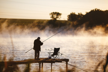 Fisher on the wooden pier to fish in the morning on sunrise. Feeder carp fishing.