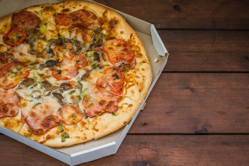 Italian pizza in a cardboard box. Pizza on wooden background in rustic style. Simple food on a wooden background. Tasty dish for lunch