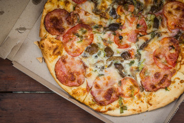 Italian pizza in a cardboard box. Pizza on wooden background in rustic style. Simple food on a wooden background. Tasty dish for lunch