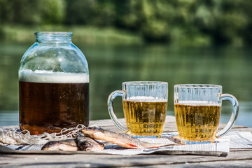 Beer in a jar and in mugs with dried fish on the pier near the river