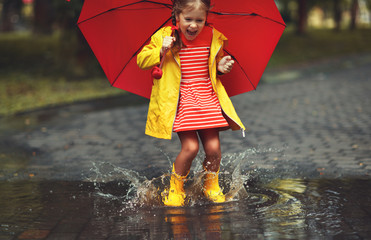 happy child girl with an umbrella and rubber boots in puddle  on autumn walk