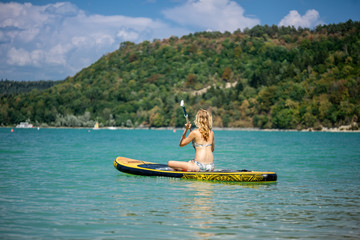 une jeune femme blonde de dos, rame sur un paddle, assise.