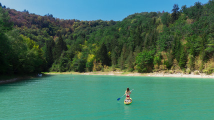 une jeune fille de dos sur son stand up paddle jaune, au milieu d'eau verte